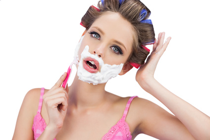 Model in hair curlers shaving her face and looking at camera on white background